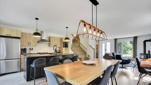 A modern kitchen with a central island, a dining area with a wooden table, and a staircase leading to an upper level.