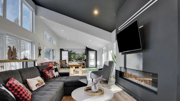 A modern living room with a fireplace, a flat-screen TV, and a dining area visible through an open door.
