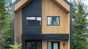 A modern two-story house with a prominent gable roof, large windows, and a wooden front porch.