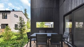 A modern outdoor patio with a table and chairs, a view of a neighboring building, and a wooden deck.