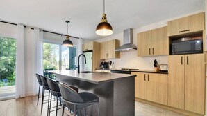 A modern kitchen with a central island, bar stools, pendant lighting, and wooden cabinets.
