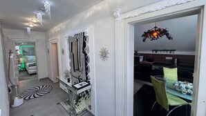 A hallway with a mirror, a dining area with a green chair, and a kitchen visible through an open door.