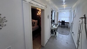 A hallway with a bed, a mirror, a chandelier, and a hairdryer.