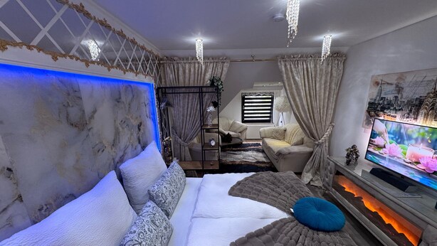 A modern bedroom with a large bed, a TV, and a fireplace.