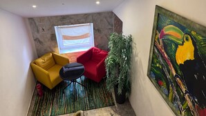 A compact living space with a red sofa, a yellow armchair, a small table, a potted plant, and a large painting of a toucan.
