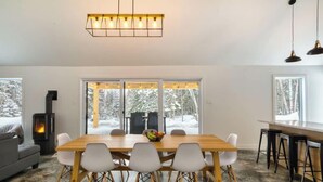 Ein modernes Interieur mit einem Esstisch, Stühlen, einem Kamin und großen Fenstern.