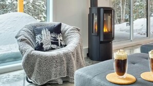 Ein gemütliches Zimmer mit Kamin, einem Sessel mit Decke und zwei Gläsern eines dunklen Getränks auf einem Tisch.
