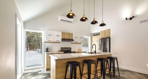 Una cocina moderna con una isla central, taburetes de bar, iluminación colgante y vistas al exterior.