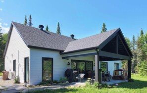 Une maison de plain-pied avec un porche couvert, un barbecue et une petite maison de jeu.