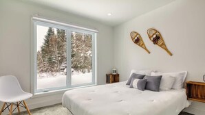 Ein Schlafzimmer mit einem großen Fenster, einem Bett mit weißer Bettwäsche, zwei Nachttischen und einem weißen Sessel.