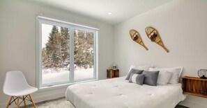 A bedroom with a large window, a bed with white bedding, two nightstands, and a white chair. - Cocotte d'hiver Animaux bienvenus  Cozy Spa (Petite-Rivière-Saint-François)