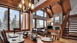 A dining area with a wooden table set for four, a fireplace, and large windows offering a view of trees. - Alpha-O | Spa | Charlevoix par Alchalet (Petite-Rivière-Saint-François)