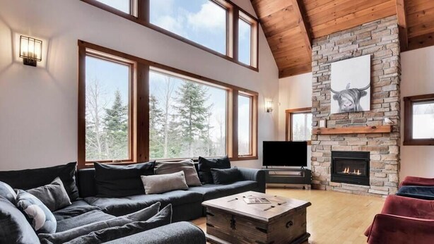A spacious living room with a large sofa, a fireplace, and a television. - Alpha-O | Spa | Charlevoix par Alchalet (Petite-Rivière-Saint-François)