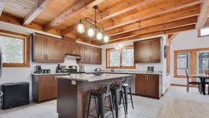 A kitchen with wooden cabinets, a central island with stools, and pendant lighting. - Alpha-O | Spa | Charlevoix par Alchalet (Petite-Rivière-Saint-François)
