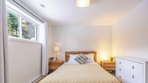 A bedroom with a bed, bedside tables, a dresser, and a window with a view of trees. - Apollon - Piscine, Spa, Sauna by Alchalet (Pont-Rouge)