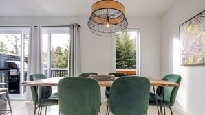 A dining area with a wooden table and green chairs, a pendant light, and a view through large windows. - Apollon - Piscine, Spa, Sauna by Alchalet (Pont-Rouge)