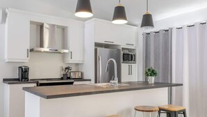 A modern kitchen with white cabinets, stainless steel appliances, a central island, and pendant lighting. - Apollon - Piscine, Spa, Sauna by Alchalet (Pont-Rouge)