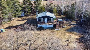 A cabin with a deck, surrounded by trees and a clear sky. - La Petite Ourse Cozy Getaway in Charlevoix  Spa (Petite-Rivière-Saint-François)