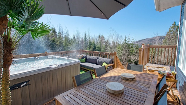 A wooden deck with a hot tub, outdoor seating, and a table with a round table runner. - La Petite Ourse Cozy Getaway in Charlevoix  Spa (Petite-Rivière-Saint-François)