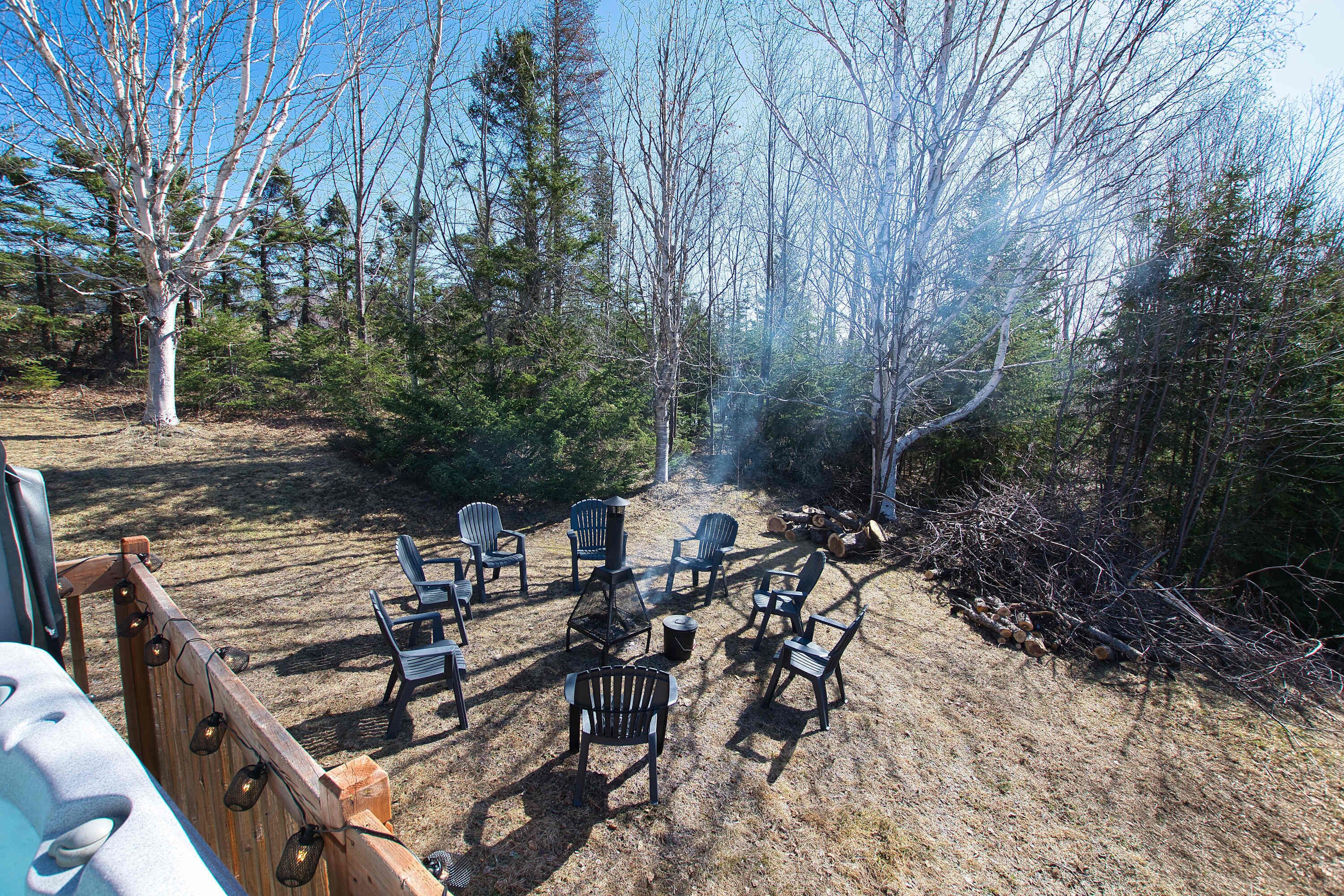 Un campeggio con diverse poltrone Adirondack disposte attorno a un braciere, circondato da alberi.