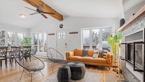 A spacious living area with a wooden ceiling, a fireplace, a sofa, and a dining table with chairs. - La Petite Ourse Cozy Getaway in Charlevoix  Spa (Petite-Rivière-Saint-François)