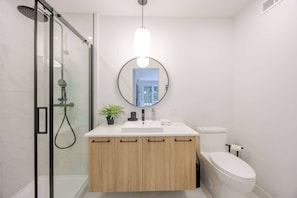 A modern bathroom with a glass shower enclosure, a round mirror, a white sink, and a toilet. - La Madeleine - Élégance en Forêt - Spa by Alchalet (Capitale-Nationale)