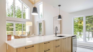 Une cuisine moderne dotée d’un grand îlot central, de meubles en bois, d’un évier et de luminaires suspendus.