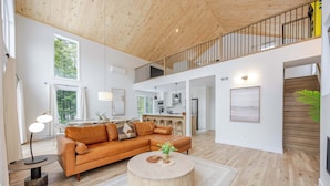 Un vaste espace de vie doté d’un plafond en bois, d’un canapé en cuir marron, d’une table basse ronde et d’un escalier menant à un niveau supérieur.
