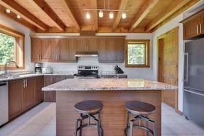 A modern kitchen with wooden cabinets, a granite countertop, and two bar stools. - Chalet l'Ascension  Nature getaway with Spa (Petite-Rivière-Saint-François)