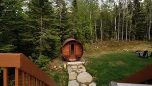 Une cabane en bois, accessible par un sentier de pierres, et entourée d’une forêt.