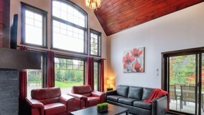 A spacious living room with a fireplace, leather sofas, and large windows offering a view of the outdoors. - Chalet charmant Vacances avec Spa by Alchalet (Scott)