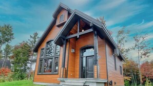 A two-story house with a prominent gable roof, large windows, and a front porch. - Chalet charmant Vacances avec Spa by Alchalet (Scott)