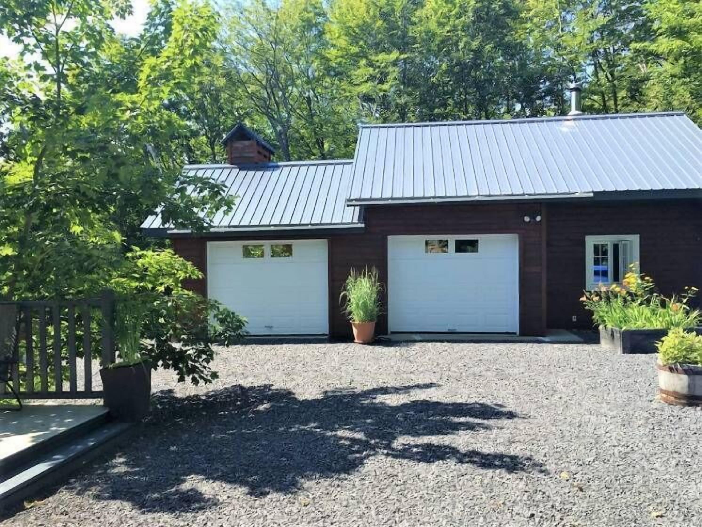 A two-story building with a metal roof, two garage doors, and a gravel driveway.
