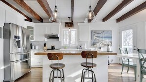 A modern kitchen with white cabinets, stainless steel appliances, a wooden island with stools, and exposed wooden beams.
