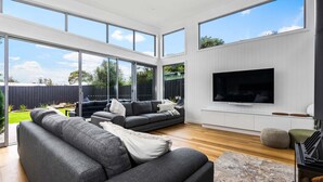 Un salon spacieux avec une grande télévision, des canapés gris et un plancher en bois.