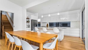 Une cuisine moderne avec des meubles blancs, une table à manger en bois et des chaises blanches.