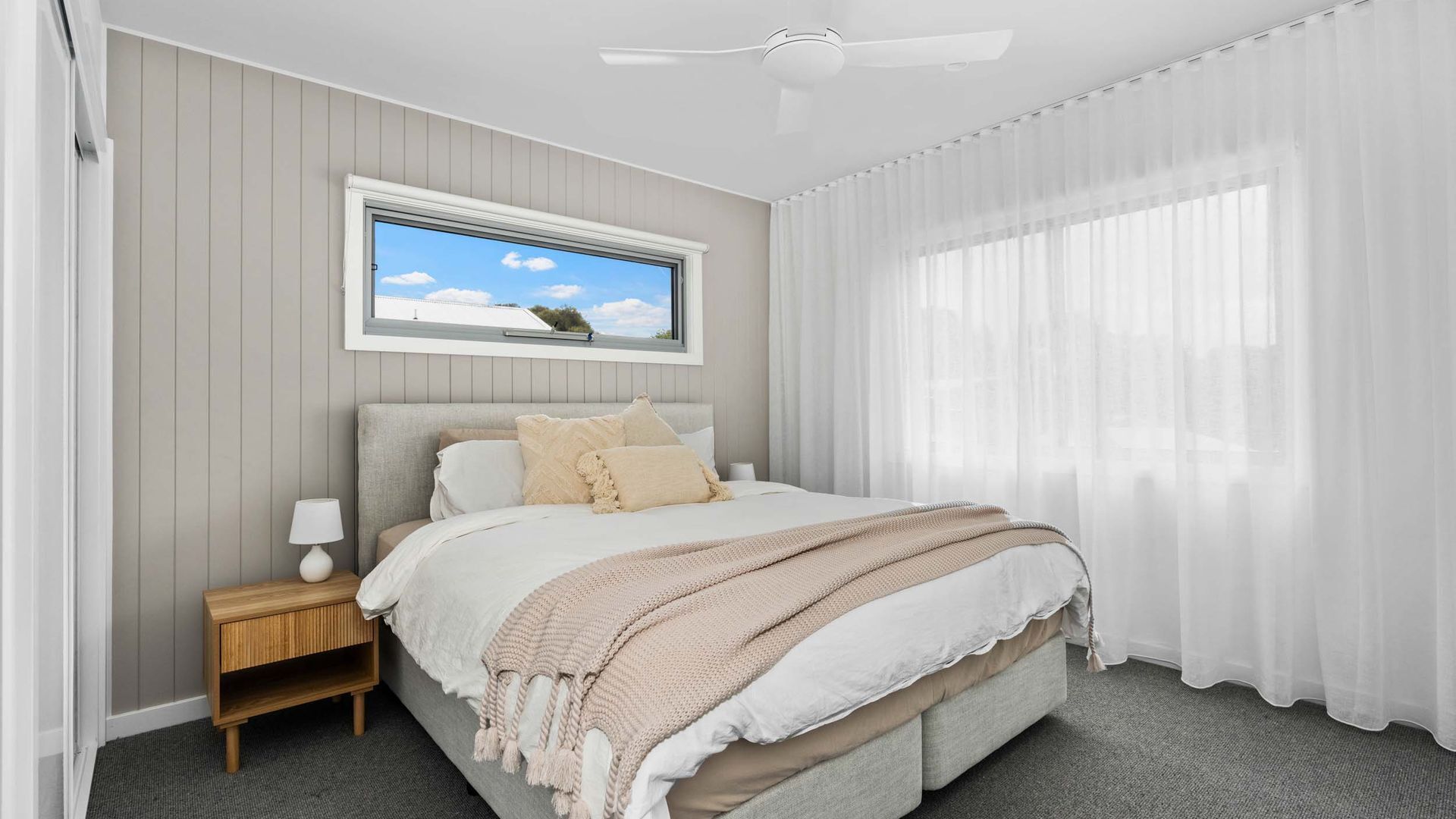 A bedroom with a bed, a nightstand, a window with a view, and a ceiling fan.