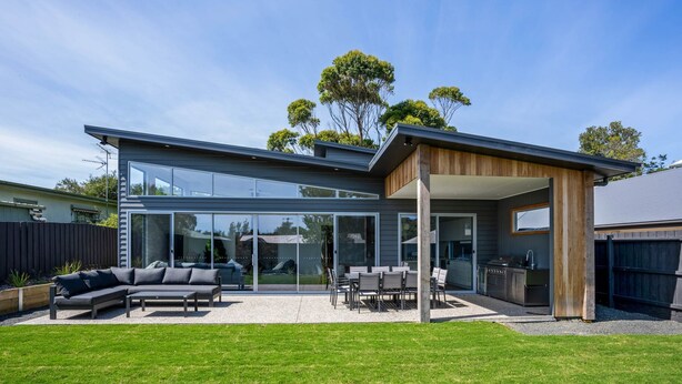 Une maison moderne dotée d’un patio entièrement vitré, de mobilier d’extérieur et d’une pergola en bois.