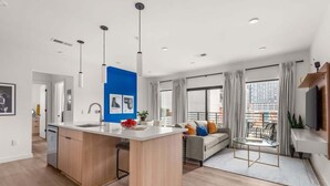 A modern apartment with a kitchen island, a dining area, a sofa, and a TV. - Jazzy Blue at HYVE | Near Gulch & Broadway (Nashville)