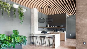 A modern kitchen with a central island, bar stools, hanging plants, and pendant lighting. - Jazzy Blue at HYVE | Near Gulch & Broadway (Nashville)