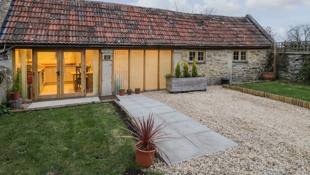 A stone building with a tiled roof, a gravel driveway, and a small garden with potted plants.