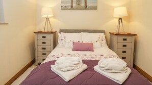 A bedroom with a bed, two bedside tables, a lamp on each table, a painting above the bed, and a window on the left.