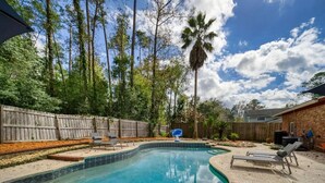 A backyard with a swimming pool, wooden fence, and lounge chairs.