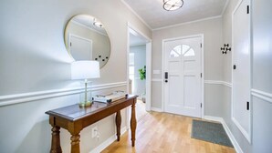 A hallway with a wooden console table, a round mirror, and a white door with a small window.