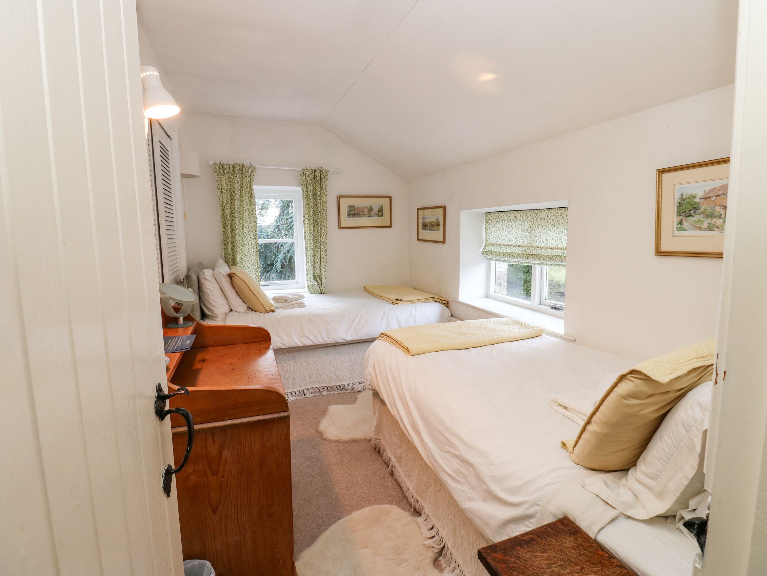 A bedroom with two beds, a wooden dresser, a mirror, and a window with curtains.