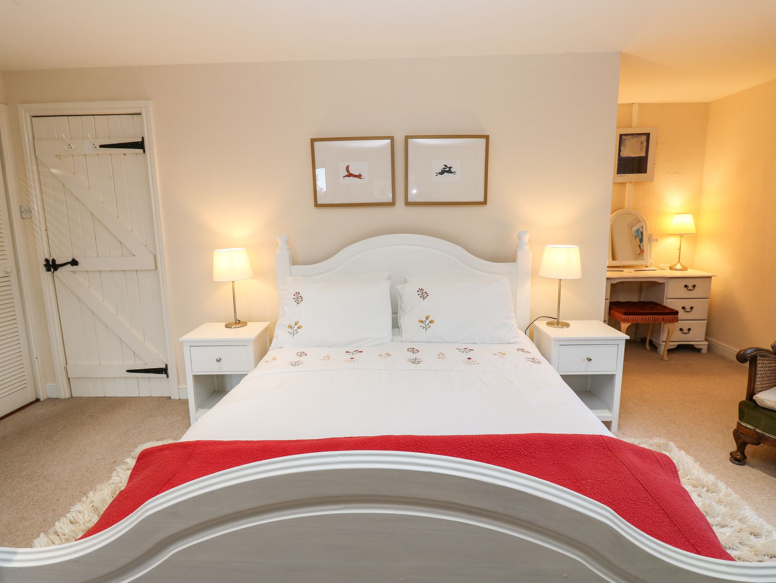 A bedroom with a white bed, two bedside lamps, a dresser, and a door with a barn-style design.