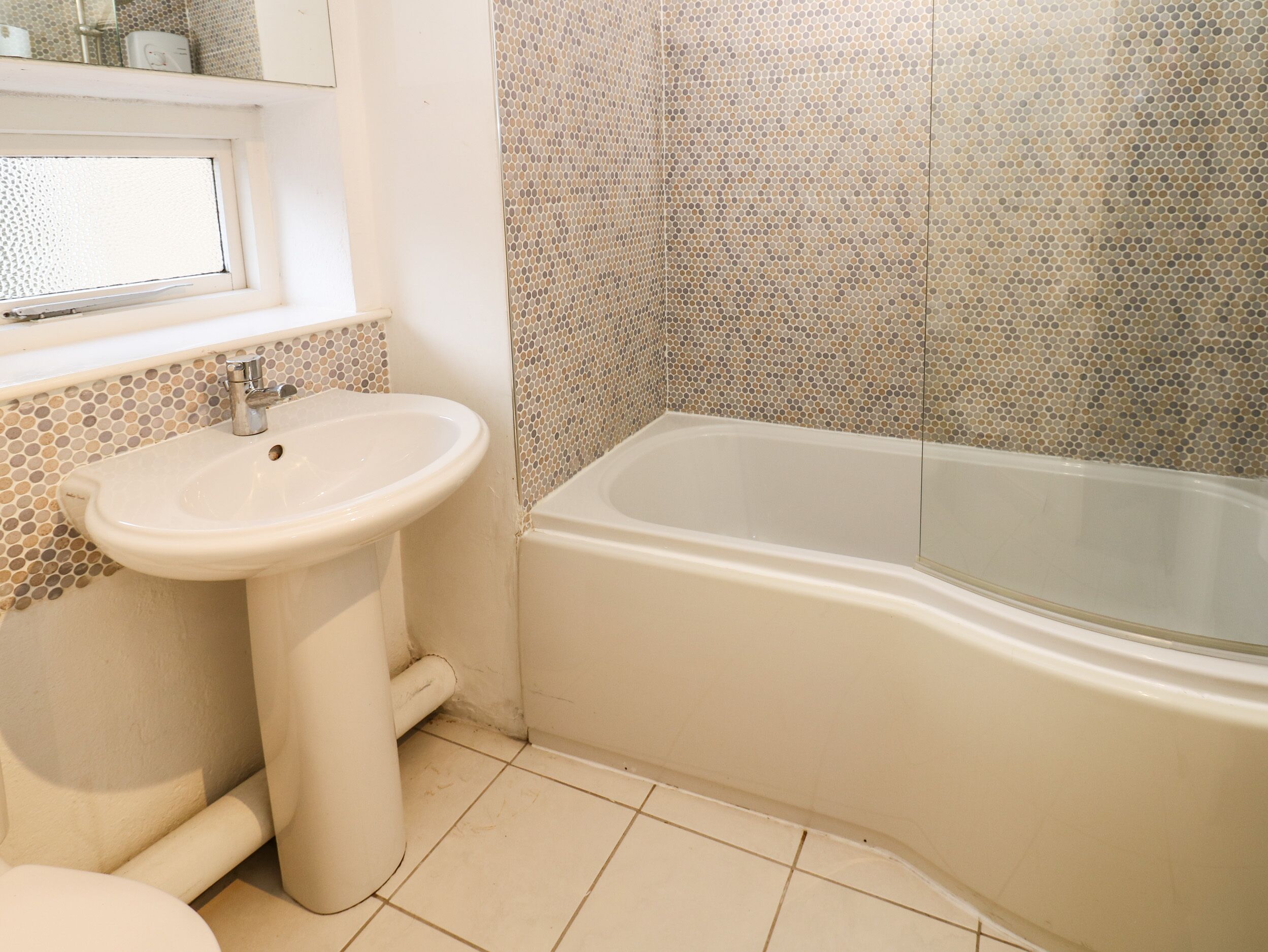 A bathroom with a white sink, a bathtub, and a tiled wall.