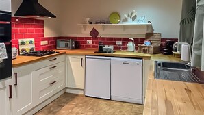 A compact kitchen with white cabinets, a red backsplash, a black range hood, and a small dishwasher. - 1 bedroom accommodation in Adversane, near Billingshurst (Adversane, near Billingshurst)
