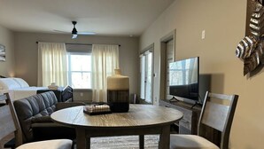 A hotel room with a bed, a sofa, a dining table with chairs, a TV, and a ceiling fan. - Choctaw Ridge King Bed-Private Deck-Gas Firepit (Dahlonega)