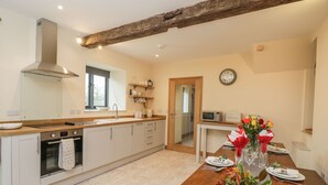 A modern kitchen with a wooden countertop, built-in oven, and a dining area with a wooden table set for four. - Chequers Barn (Corsham)